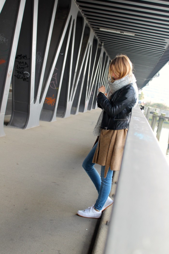 Schwarze Jacke, beiger Cardigan, helle Jeans, weiße Sneaker und grauer Schal